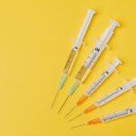 Overhead view of five syringes arranged on a yellow background.