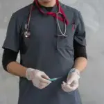 Healthcare worker with stethoscope holding a syringe ready for injection.