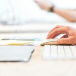A person working at a laptop with a wireless mouse and keyboard in a bright office setting.