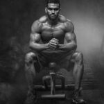 A powerful bodybuilder sitting with intense focus, showcasing muscular definition and strength.