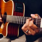 Hands playing an acoustic guitar, showcasing chords and frets up close.