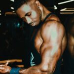 Black man demonstrating muscular physique in gym, highlighting strength and fitness.