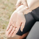 Person gripping wrist in pain, highlighting injury and support outdoors.